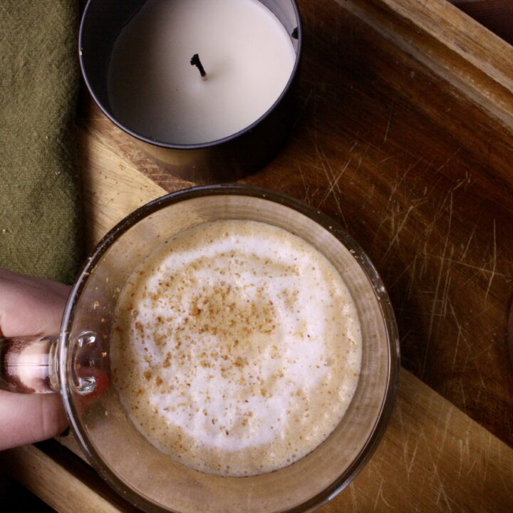 Hand holding coffee next to a candle