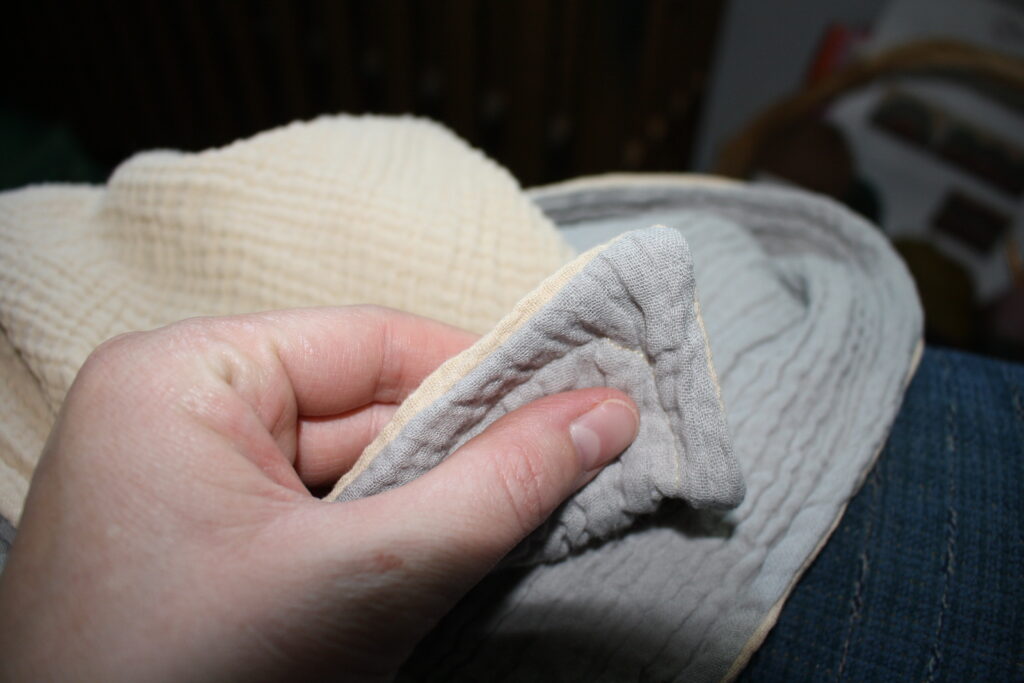 woman's hand holding the finished edge of a baby blanket sewn with cotton muslin fabric