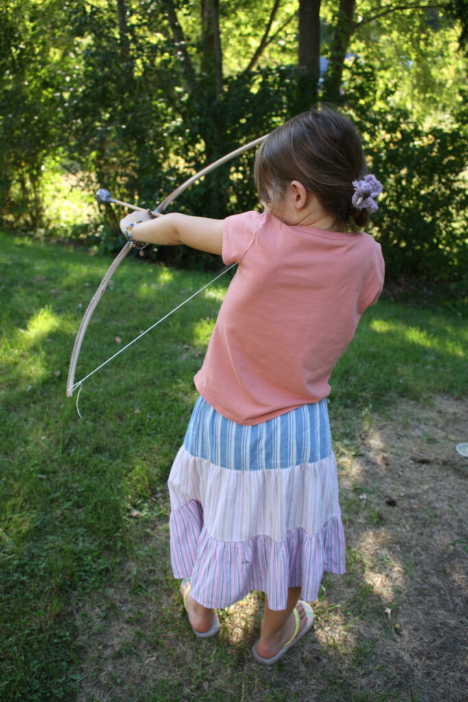 girl shooting a wooden toy bow and arrow