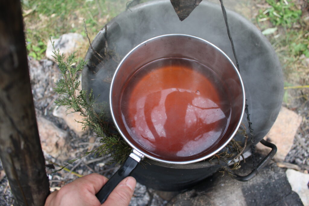 hot juniper infusion in water ladled with a pot