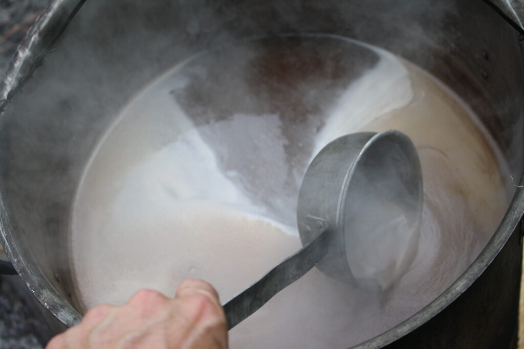 boiling wort on a fire with a hand holding a ladle to scoop off the foam