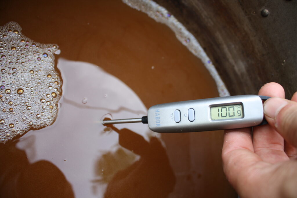 A thermometer reading 100 degrees Fahrenheit in a batch of beer wort