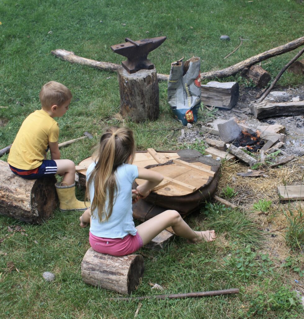 a boy and a girl working forge bellows on an open charcoal hearth