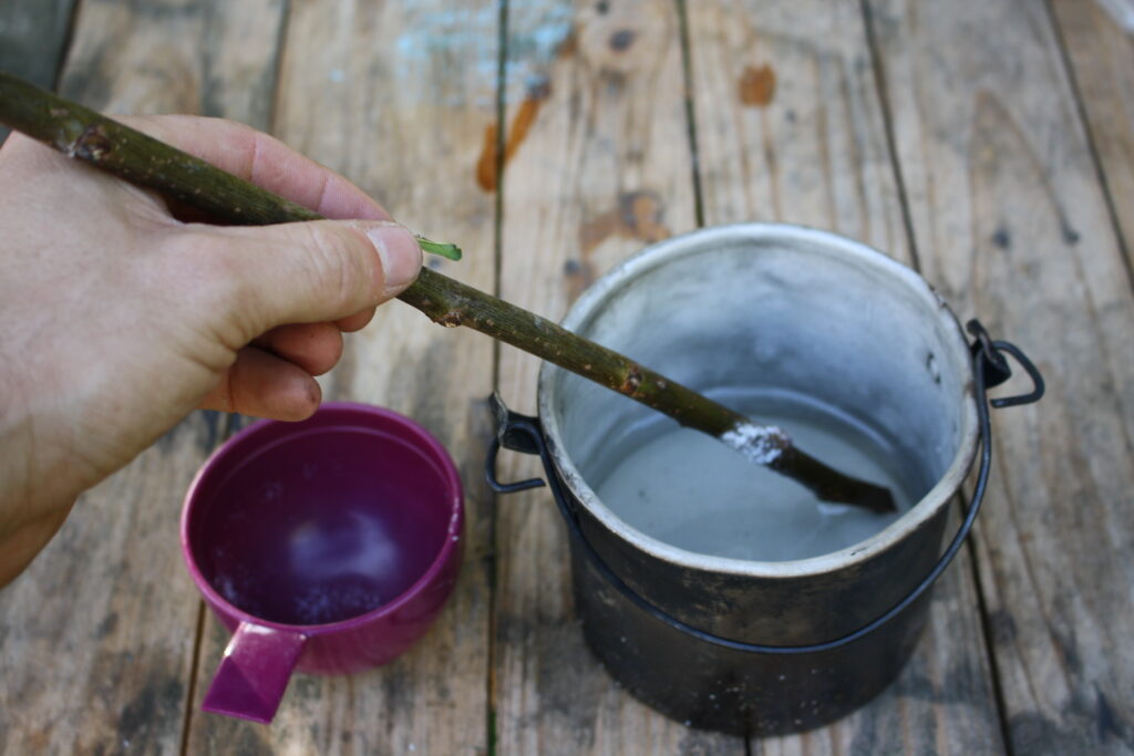 hand with a wooden stick stirring sugar into a metal pot of water