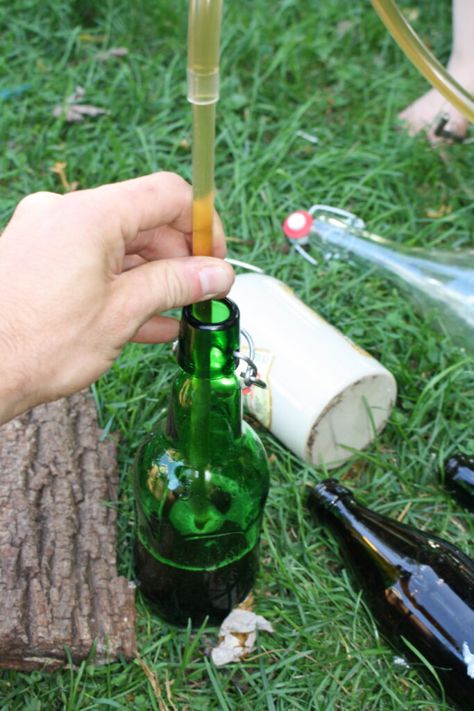 hand holding a tube filling a green glass bottle with beer