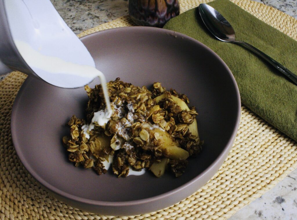 cream being poured into bowl of apple crisp