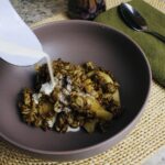 cream being poured into bowl of apple crisp