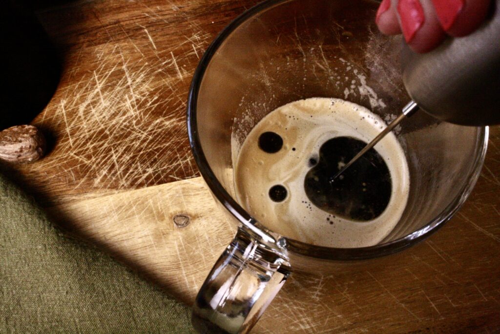 Electric whisk blending coconut oil into coffee