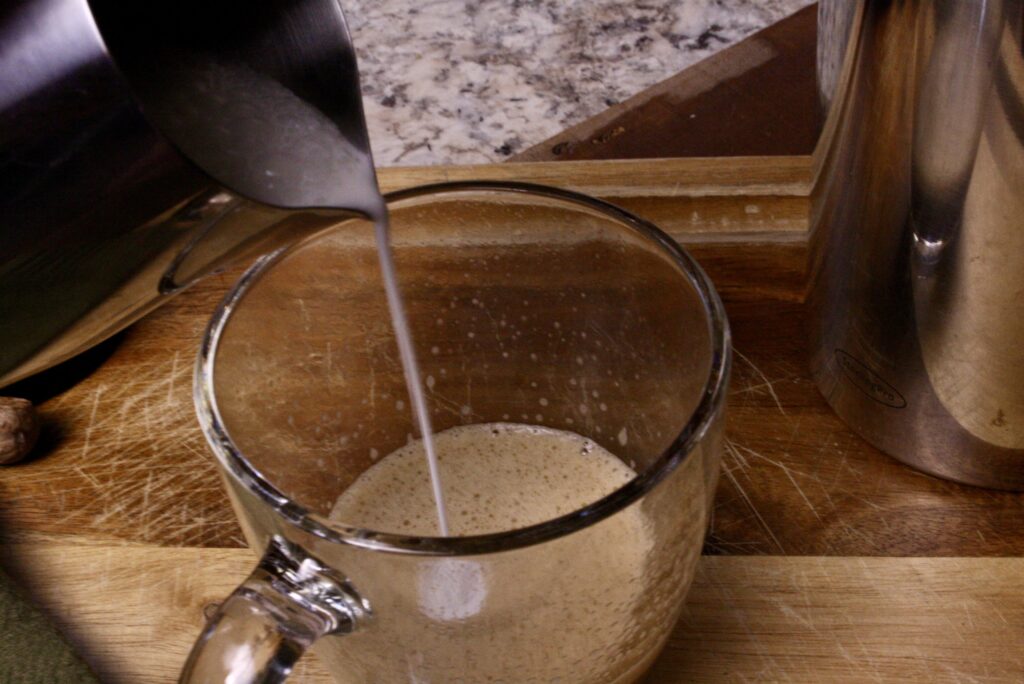 steamed milk pouring from a pitcher into cup of coffee