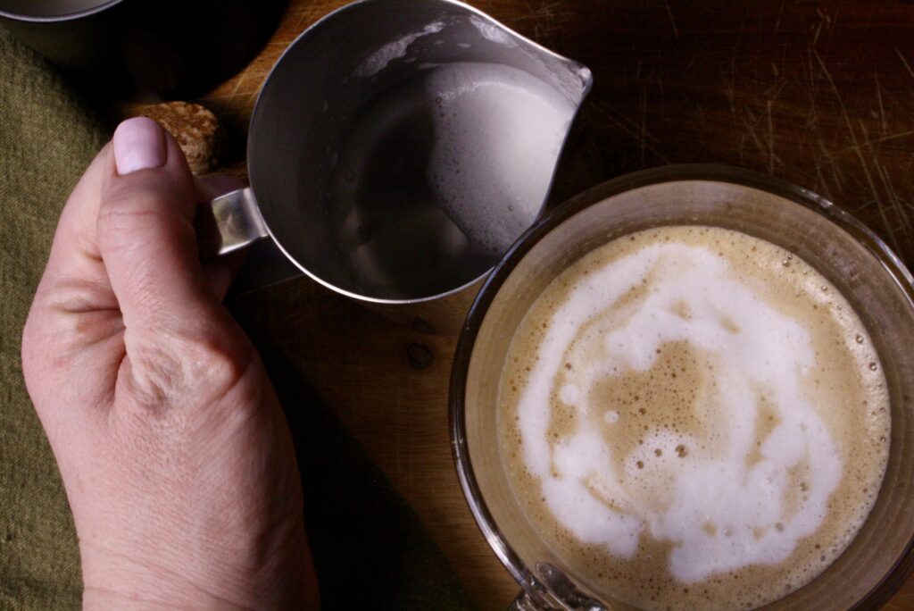 coffee and hand holding milk foaming pitcher