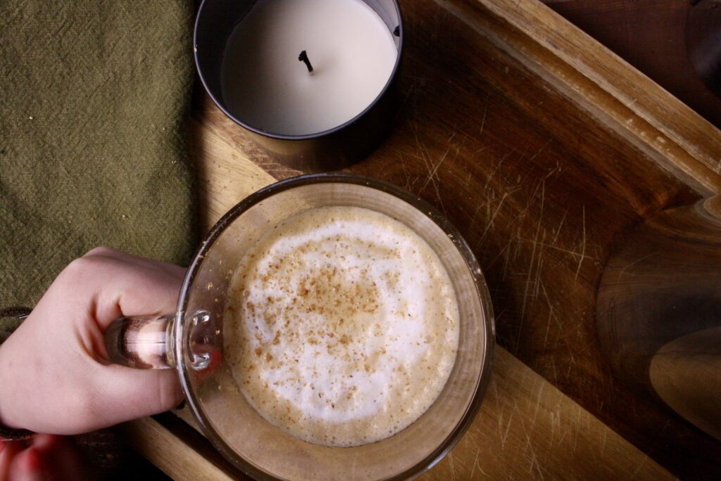 Hand holding coffee next to a candle