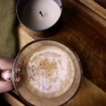 Hand holding coffee next to a candle