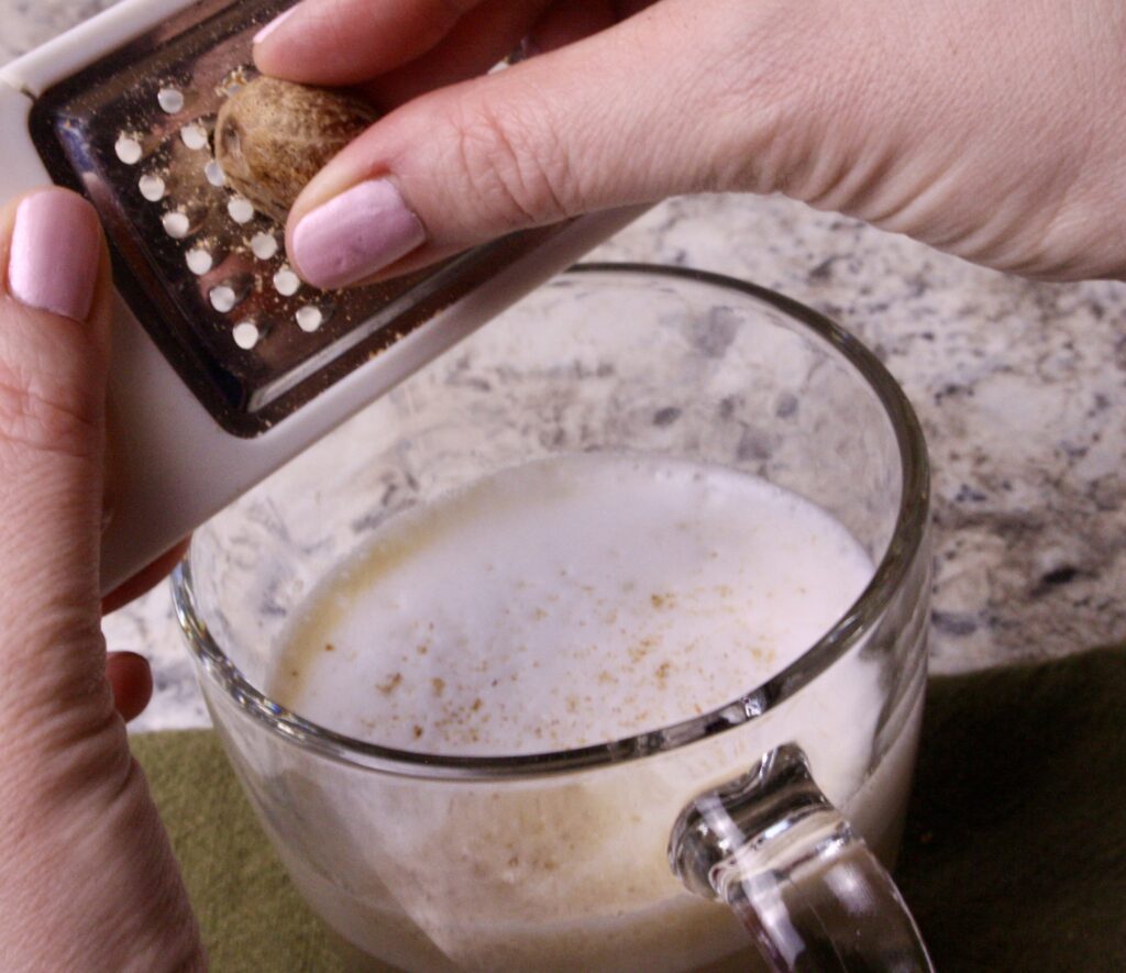 hands grating nutmeg on top of coffee foam