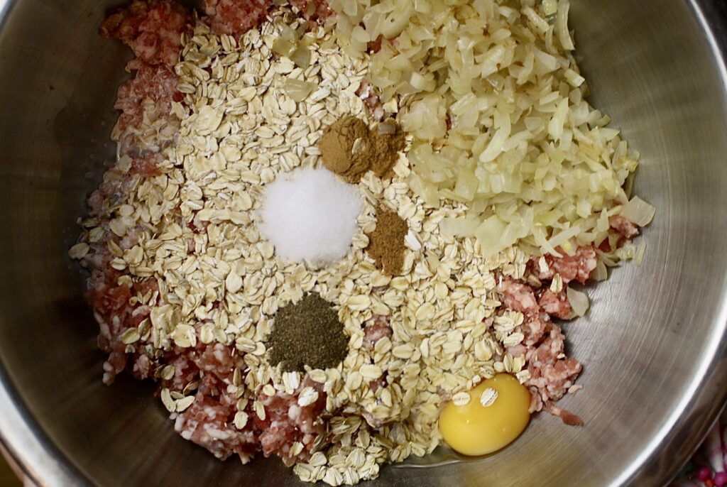 bowl of raw pork in a bowl with oatmeal, egg, onion, salt, pepper, cinnamon, and nutmeg