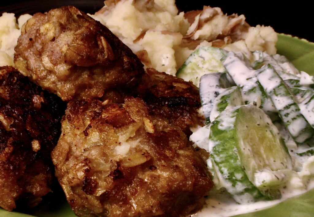 Swedish meatballs next to cucumber salad on a plate