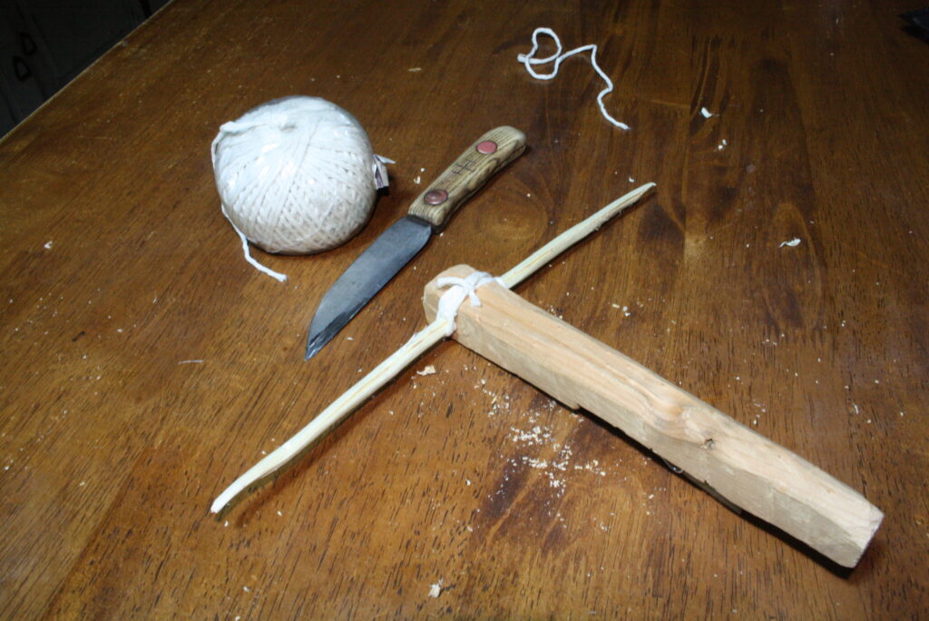 stock and bow attached with twine sitting on a table along with a knife and a ball of twine