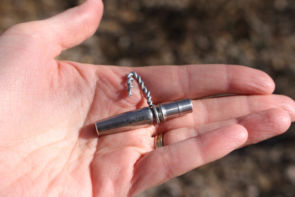 hand holding a metal maple tap with a wire hook