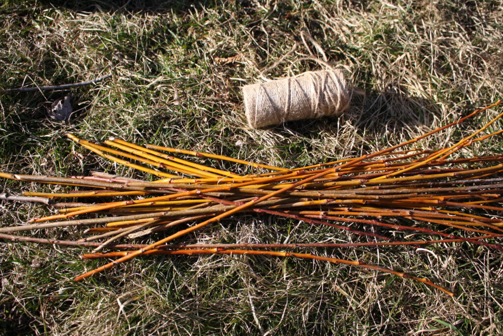 a pile of willow twigs sitting on the ground next to a spool of hemp string