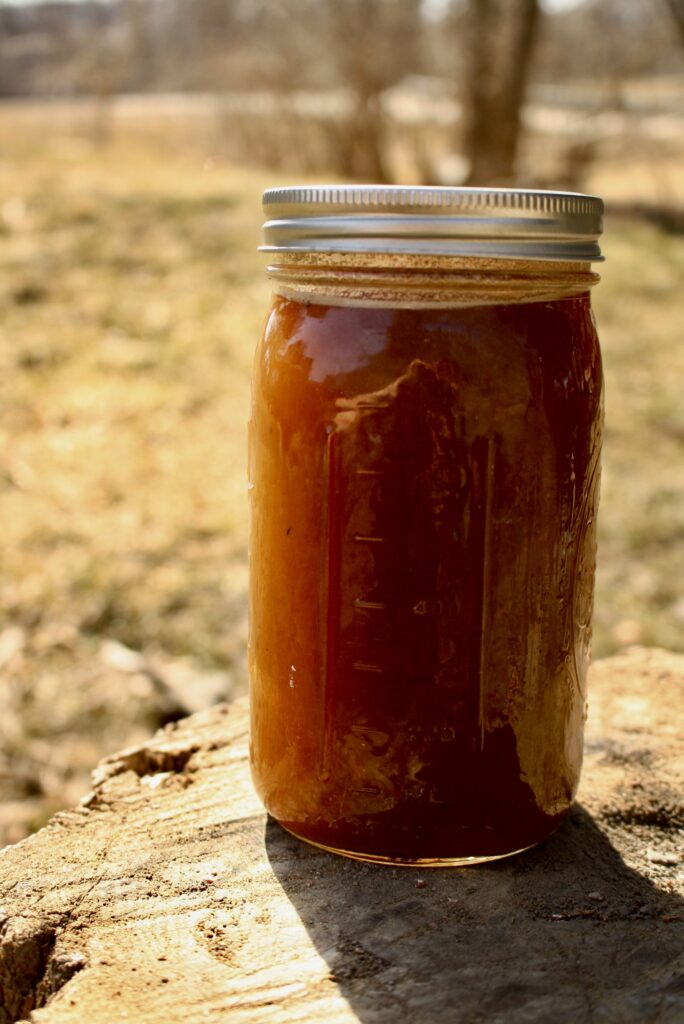 jar of freshly boiled maple syrup sitting on a stump