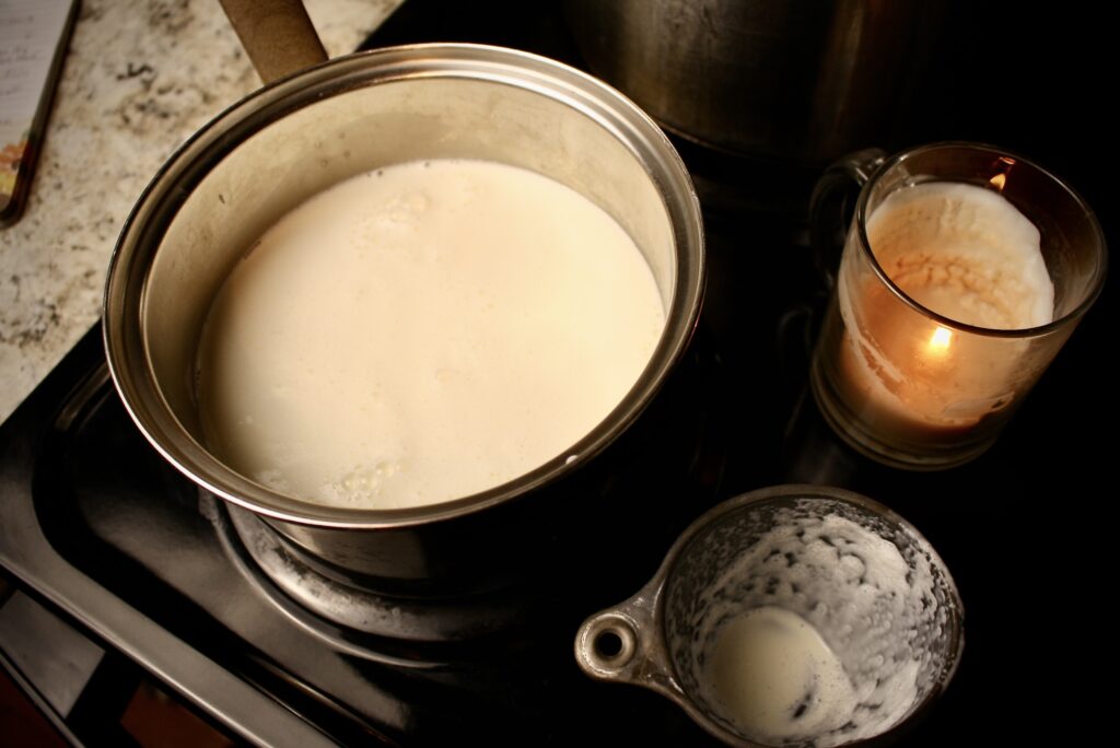 pan of milk sitting on stovetop next to measuring cup and candle