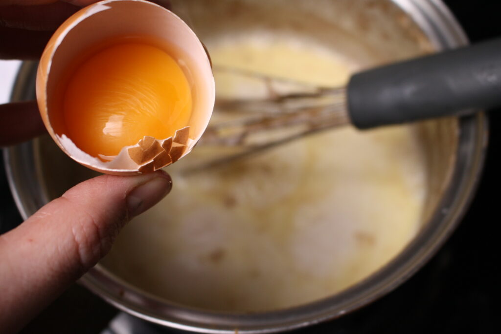 hand adding an egg to saucepan