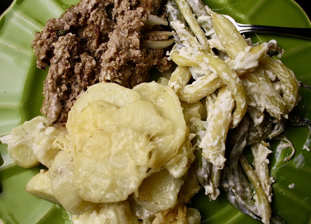 plate with creamy scalloped potatoes, green beans, and meat