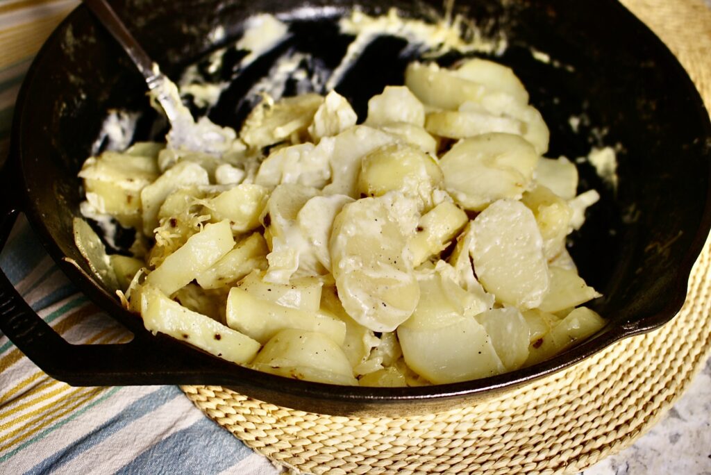 spoon in cast iron skillet with creamy scalloped potatoes