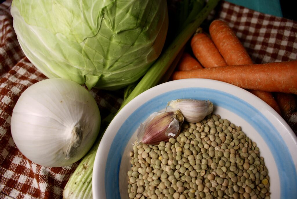 lentils, garlic, onion, cabbage, celery, and carrots sitting on a gingham towel