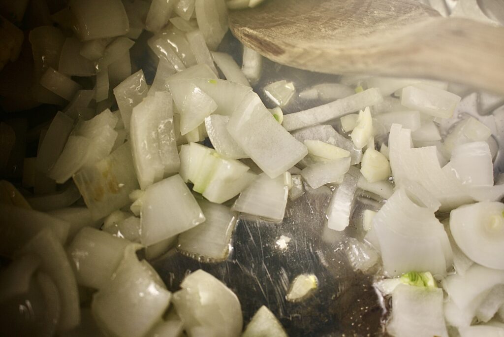 onions and garlic sautéing in a pan with a wooden spoon