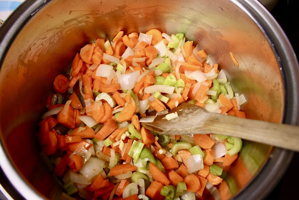 wooden spoon stirring celery, carrots, onions, and garlic in a pan