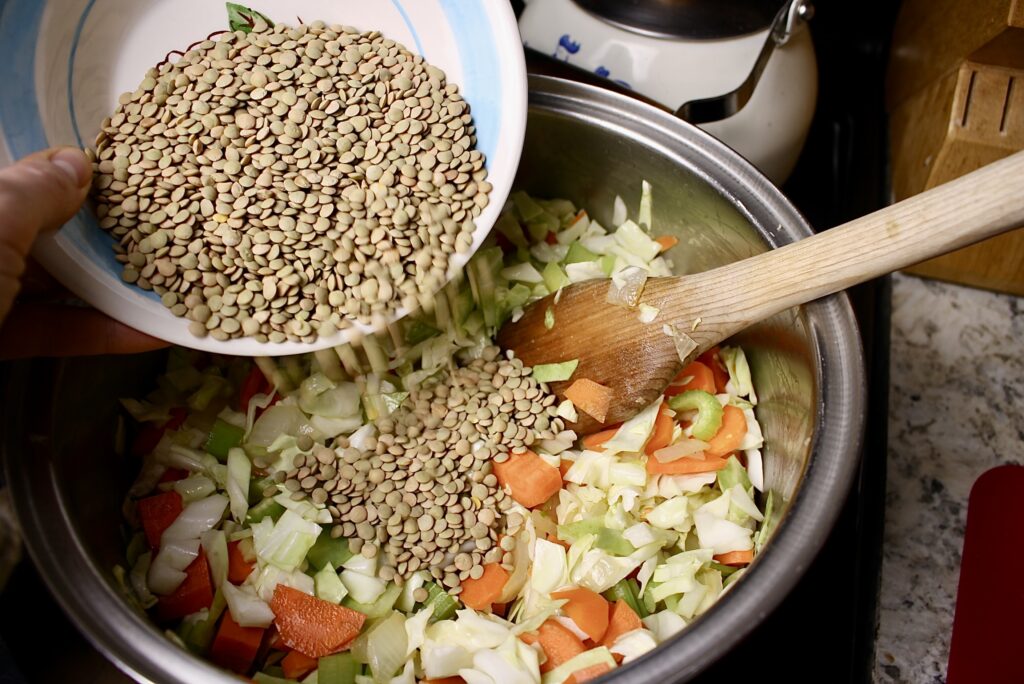 hand dumping dried lentils into a pot of veggies