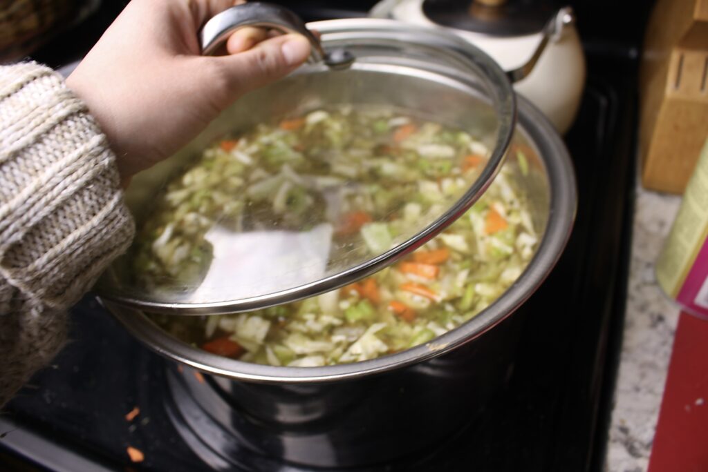 hand putting a lid on a pot of soup