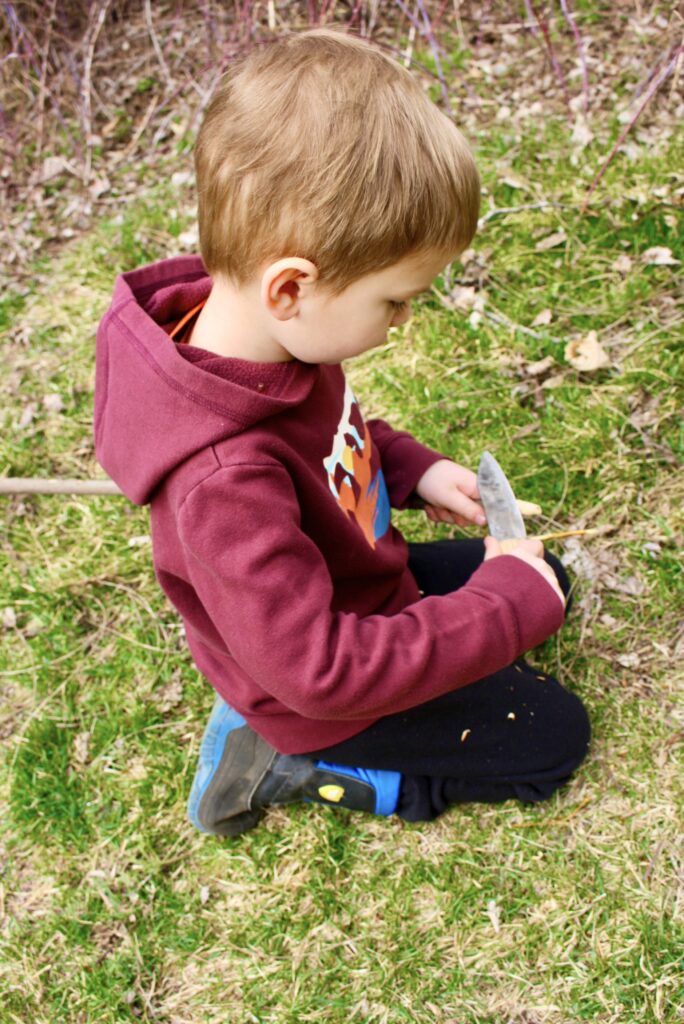 boy in a red sweater whittling a stick with a knife