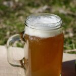 a glass mug of small beer sitting on a wooden board