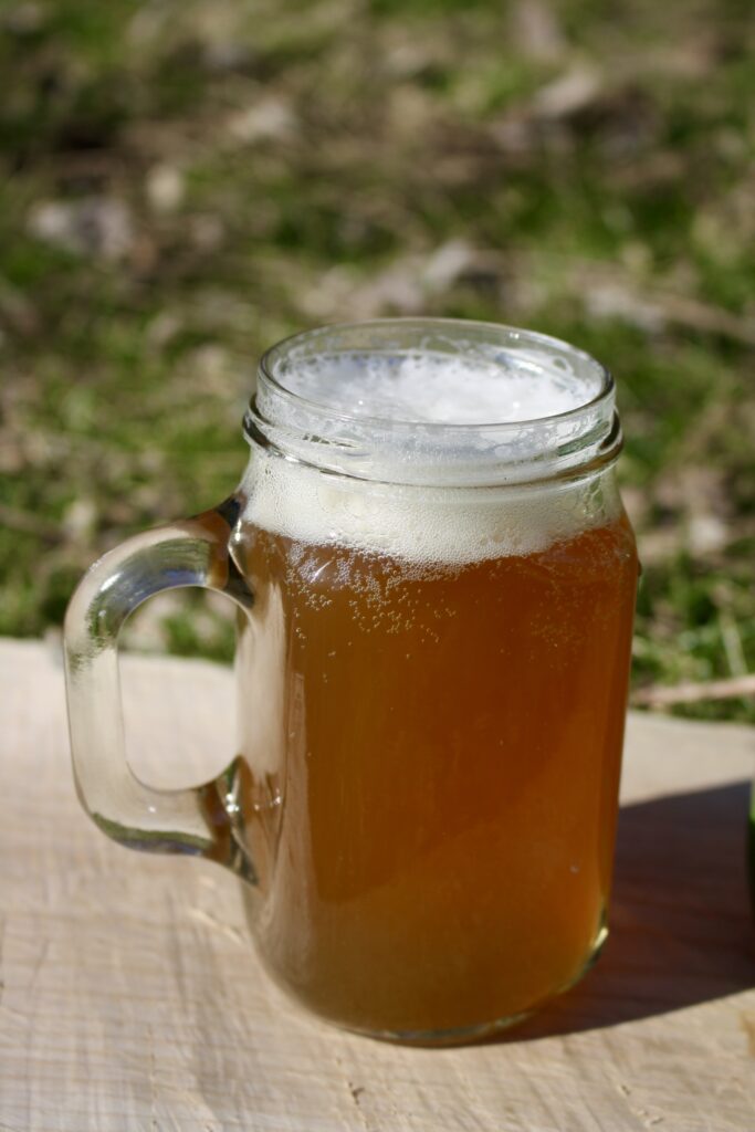 a glass mug of small beer  sitting on a wooden board