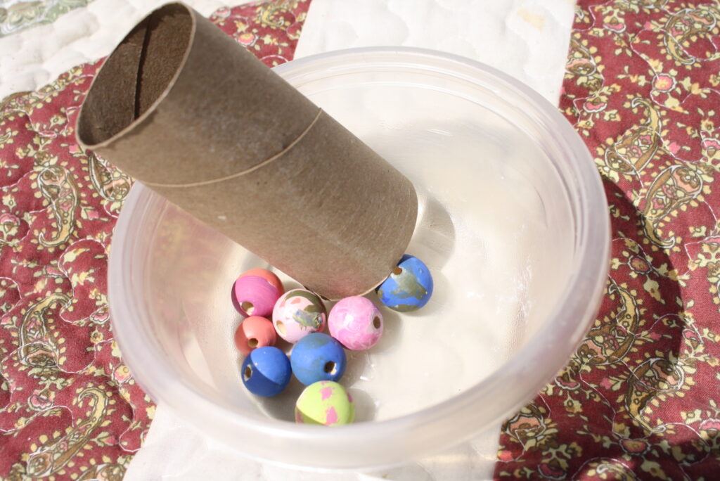 wooden beads and empty toilet paper roll in a plastic bowl