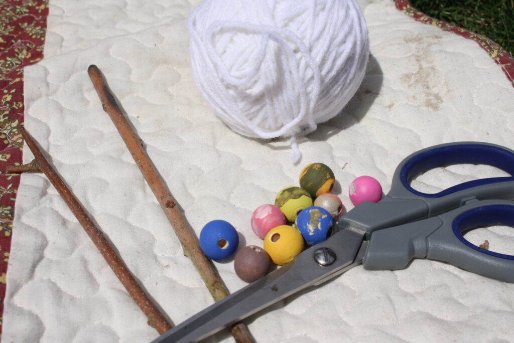 sticks, scissors, ball of yarn, wooden beads on a quilt