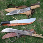 three different machetes laying on sheaths on the ground