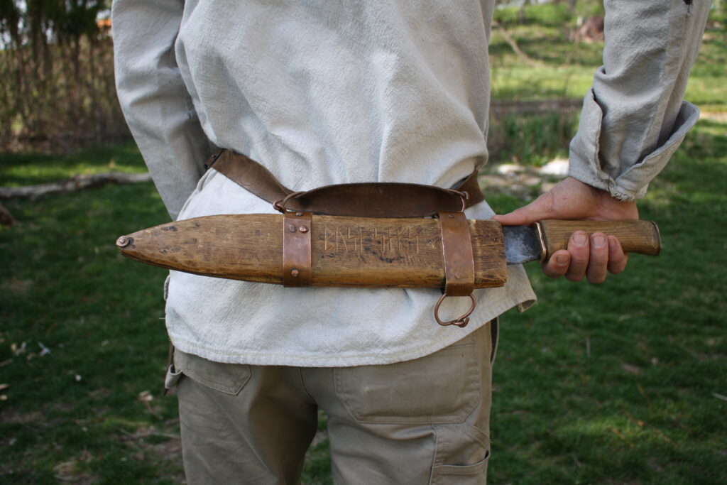 a bush-knife/machete hanging on a belt from the waist of a man with a white shirt