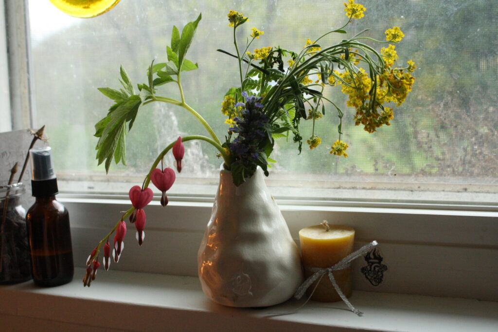 vase of spring flowers on windowsill next to beeswax candle