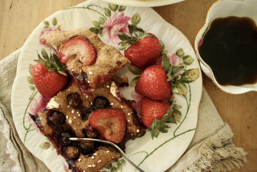 berry sourdough focaccia on a plate with strawberries next to a cup of coffee