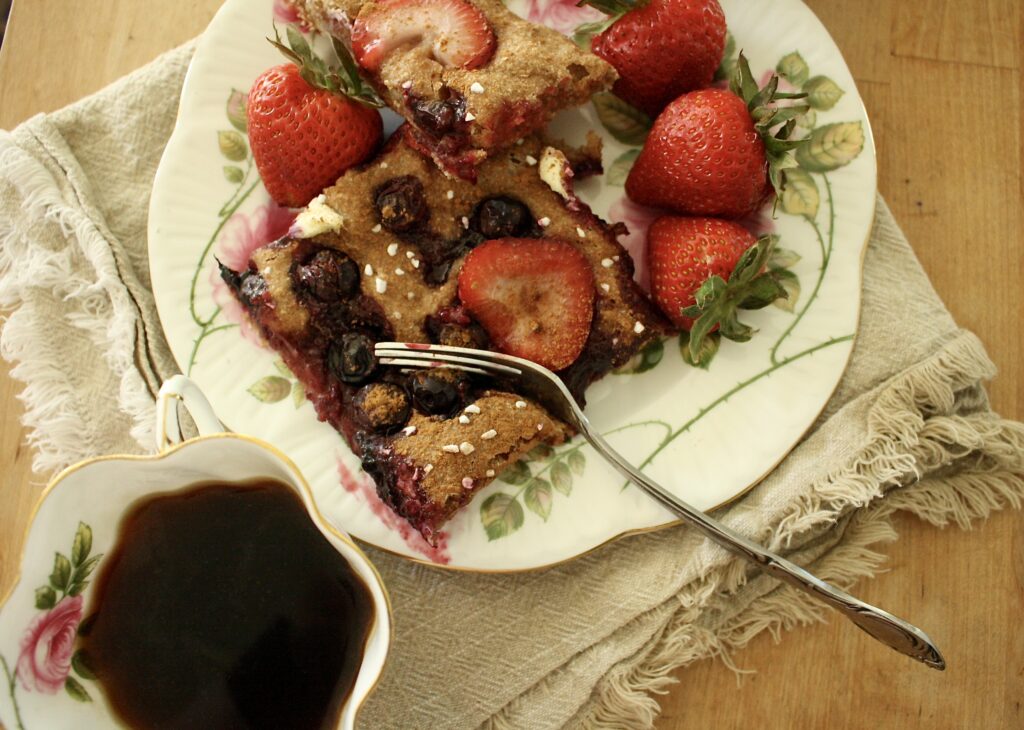 berry sourdough focaccia with strawberries on a plate next to a cup of coffee