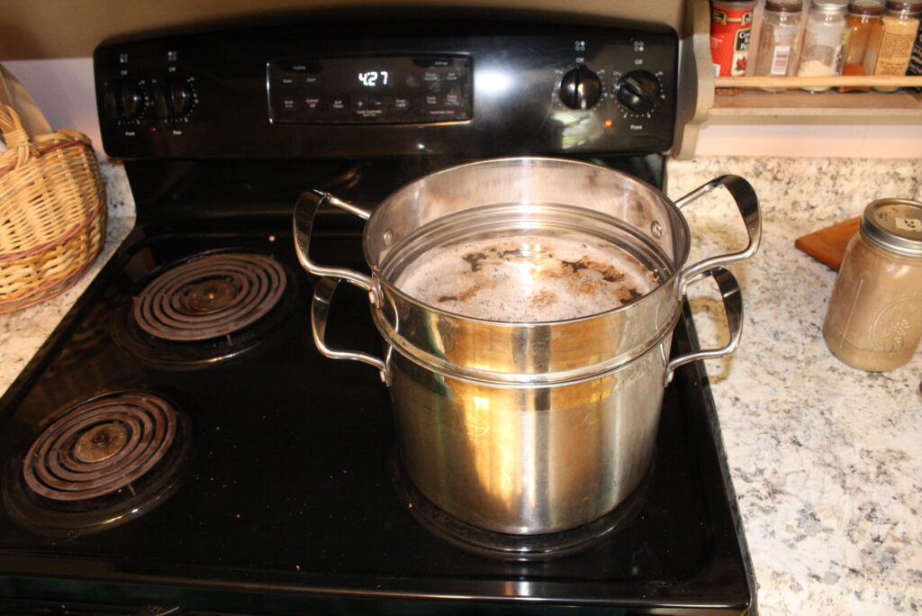 metal pot and strainer on the stovetop with spent grains brewing for making gruit 