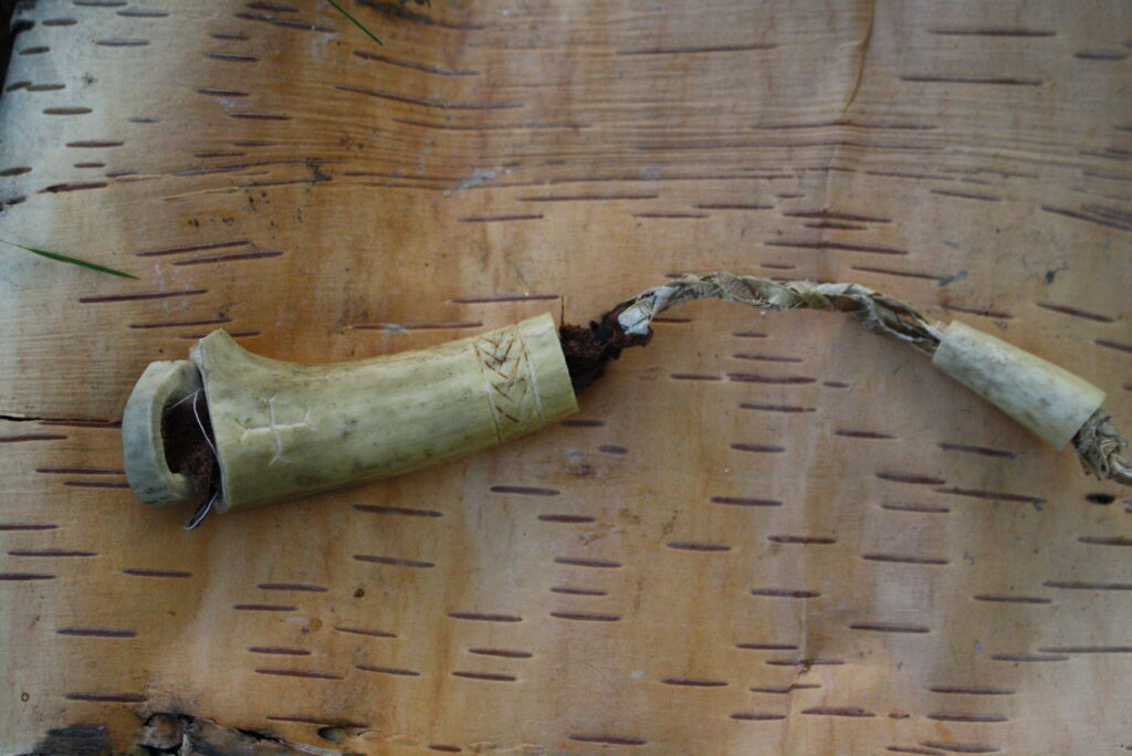 A Sami Sewing kit made from a deer antler sitting on a piece of birch bark