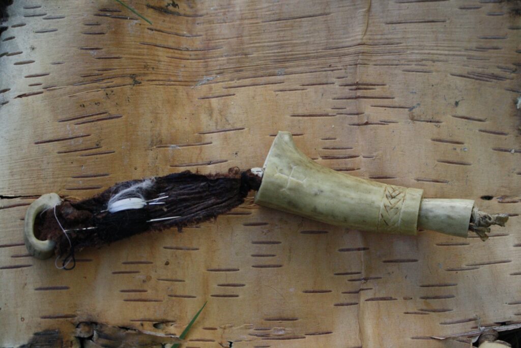 a sewing kit of deer antler sitting on a piece of birch bark showing the needles and thread.