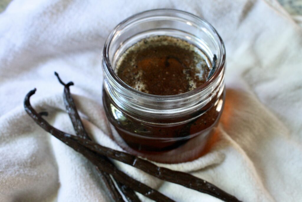 glass jar of vanilla simple syrup next to vanilla beans