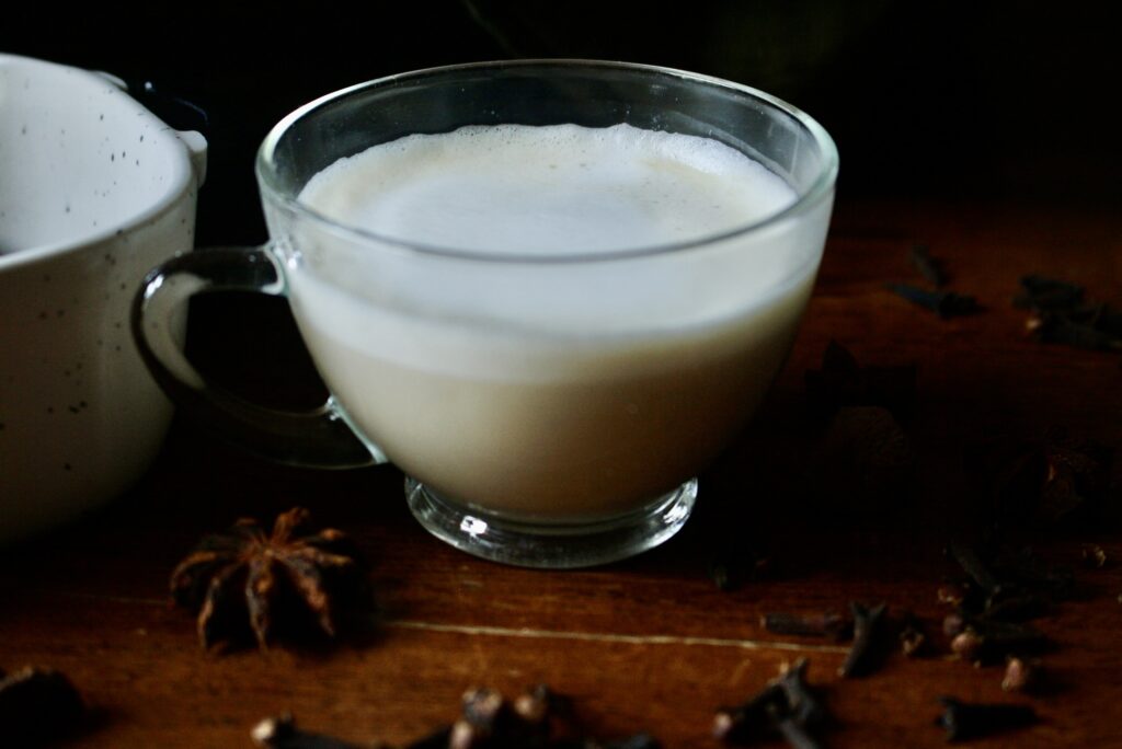 chai latte next to spices in a clear coffee mug