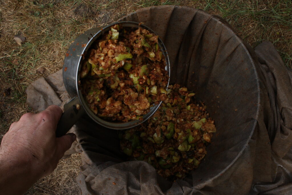 a hand scooping up crushed apple pulp with a metal sauce-pan