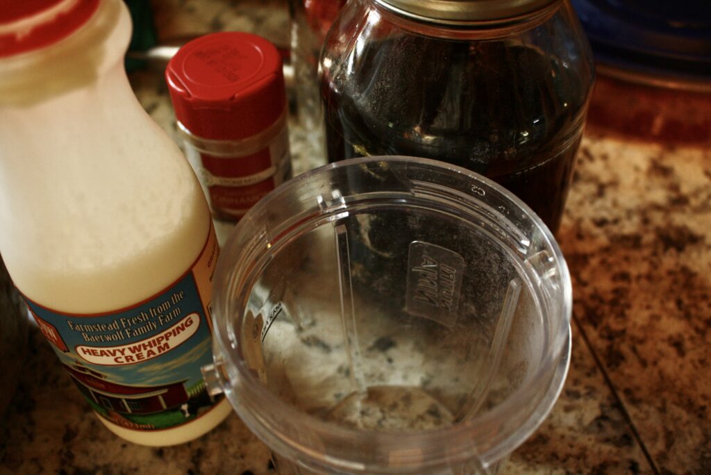 blender cup with heavy whipping cream, cinnamon, and maple syrup on the counter