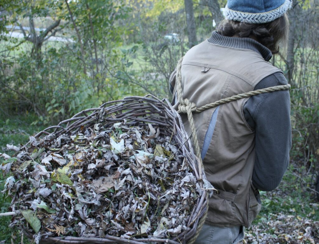 a man carrying a wicker basket on his back full of dead autumn leaves